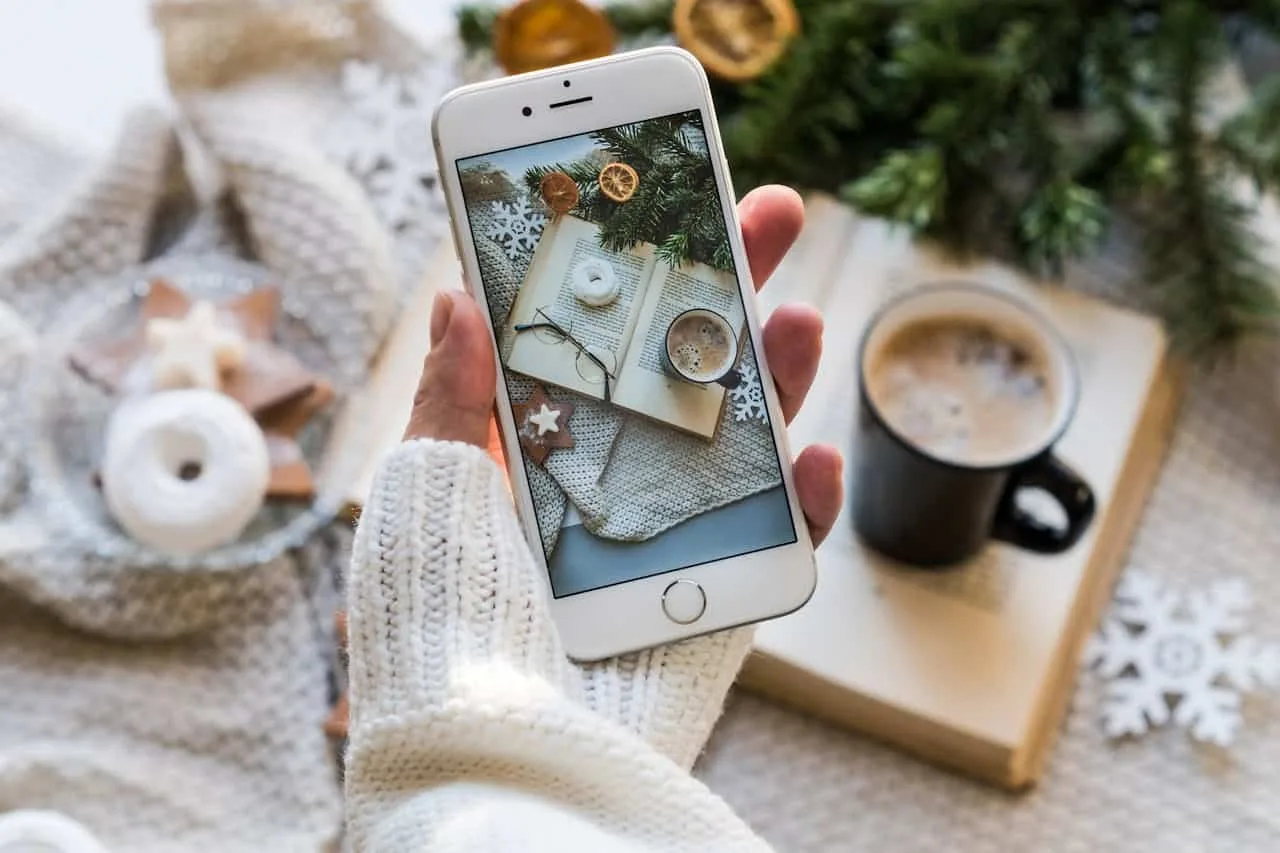 User holding an iPhone, with the camera open, about to photograph his coffee table and his book.