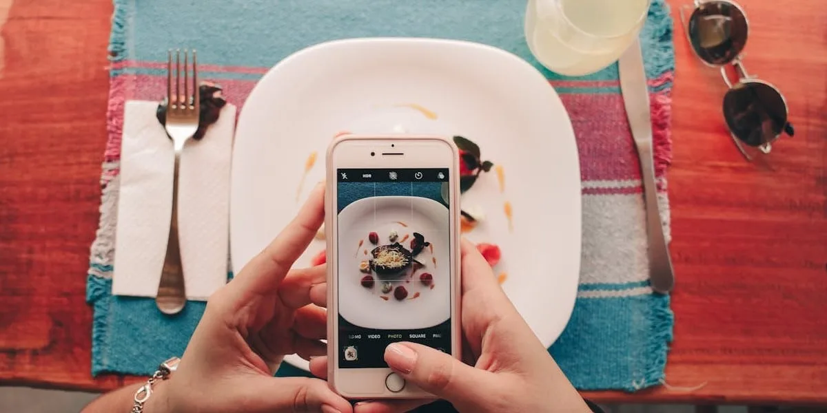 A person holding a cell phone with the Instagram camera on, taking a picture of their meal at a restaurant. Photo taken from a top angle.