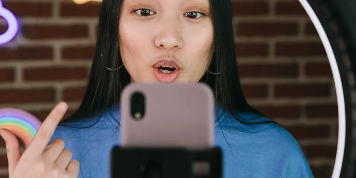 Mulher jovem, vista de frente, atrás do seu celular em um apoio no alto, enquanto grava um vídeo.