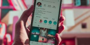 Homem segurando celular com tela ligada em seu perfil do Instagram, mostrando foto, nome de usuário e bio.