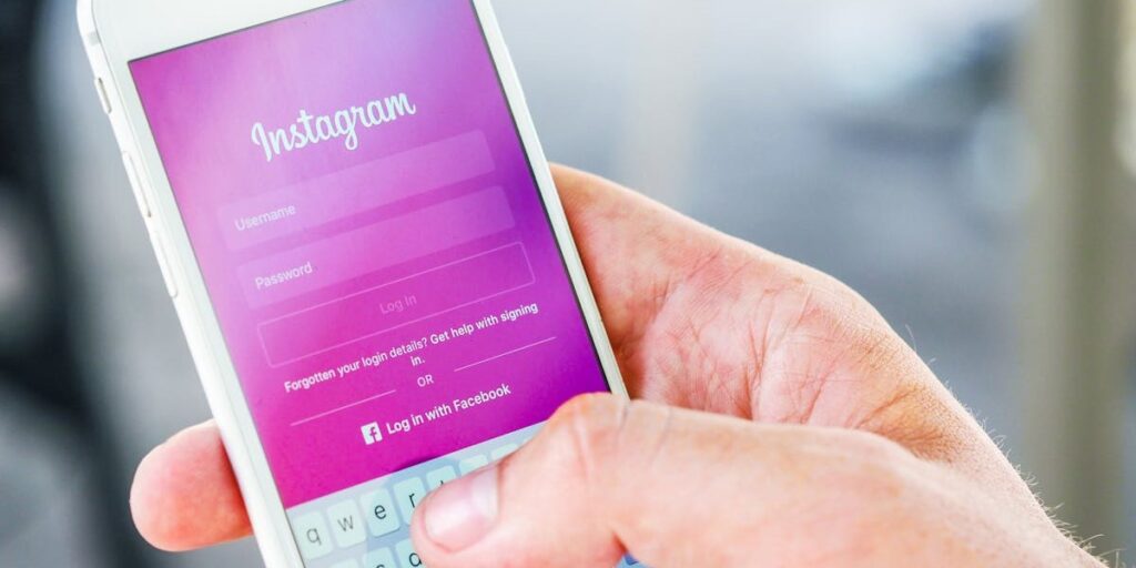 Celular branco aberto na tela de login do Instagram, que está cor de rosa, com usuário digitando sua senha para entrar na conta. Como colocar senha no Instagram?