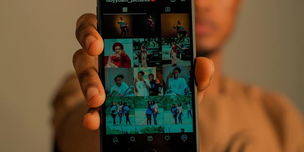Jovem rapaz segurando celular aberto no seu perfil no Instagram, mostrando várias fotos. Ele segura o celular mostrando para a câmera. Como desarquivar foto do Instagram.