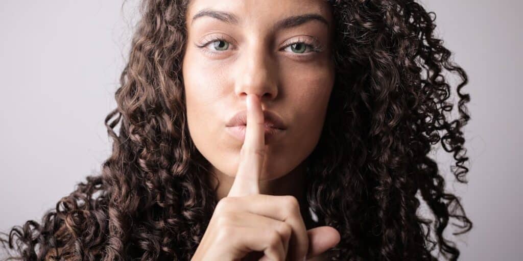 Mulher fazendo sinal de silêncio, indicando segredo, com dedo indicador estendido sobre a boca. Como desativar o modo temporário do Instagram?