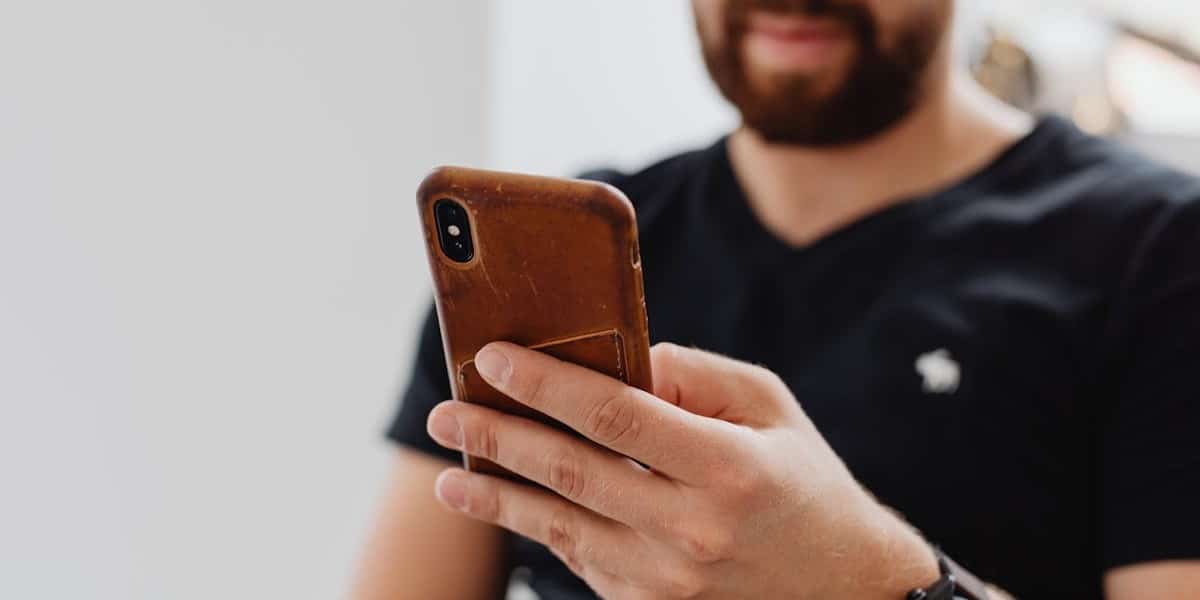 Homem jovem com barba e camisa preta, segurando celular com capa marrom. Não vemos todo o seu rosto. O fundo está é branco. Como apagar story do TikTok