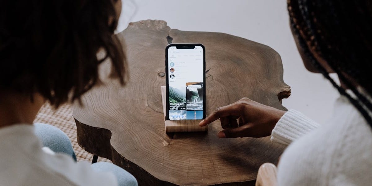 Duas pessoas, vistas de costas, escolhendo um vídeo para assistir no celular em um suporte sobre uma mesa. Quanto o TikTok paga por 1 milhão de visualizações?