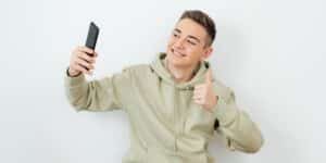 Jovem rapaz de blusa de moletom e cabelo curto, tirando foto uma selfie postar no Instagram. Como postar foto no Instagram.