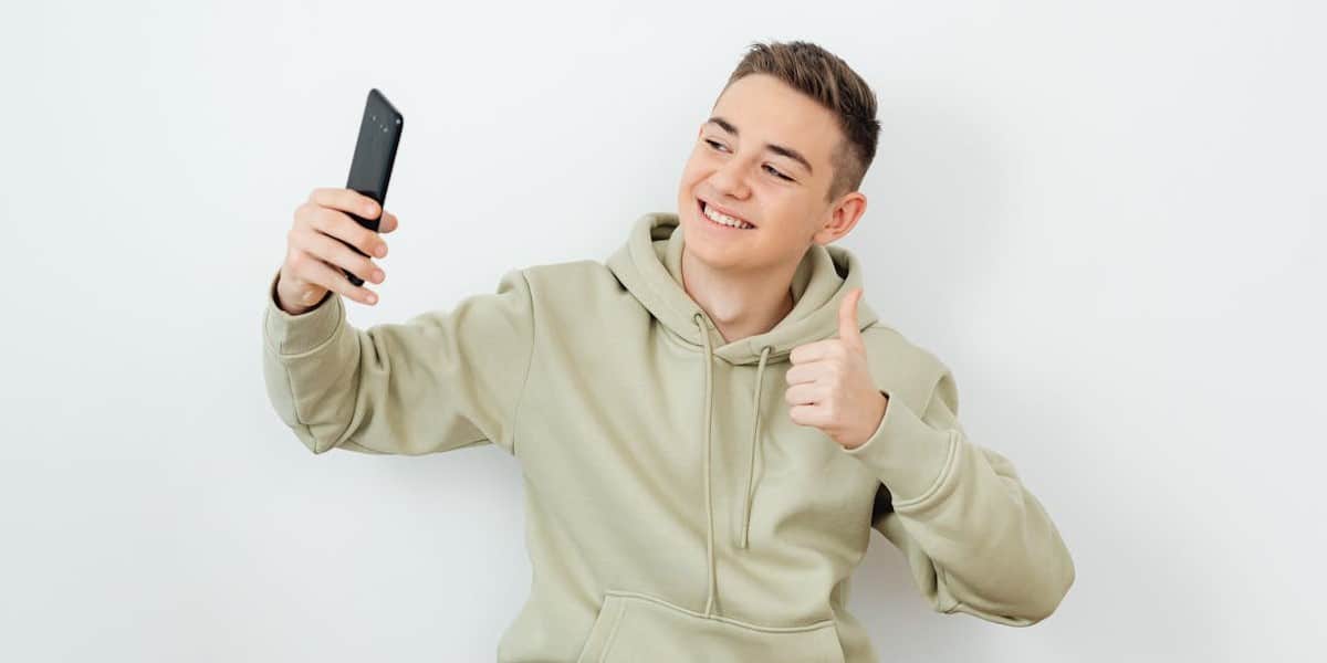 Jovem rapaz de blusa de moletom e cabelo curto, tirando foto uma selfie postar no Instagram. Como postar foto no Instagram.