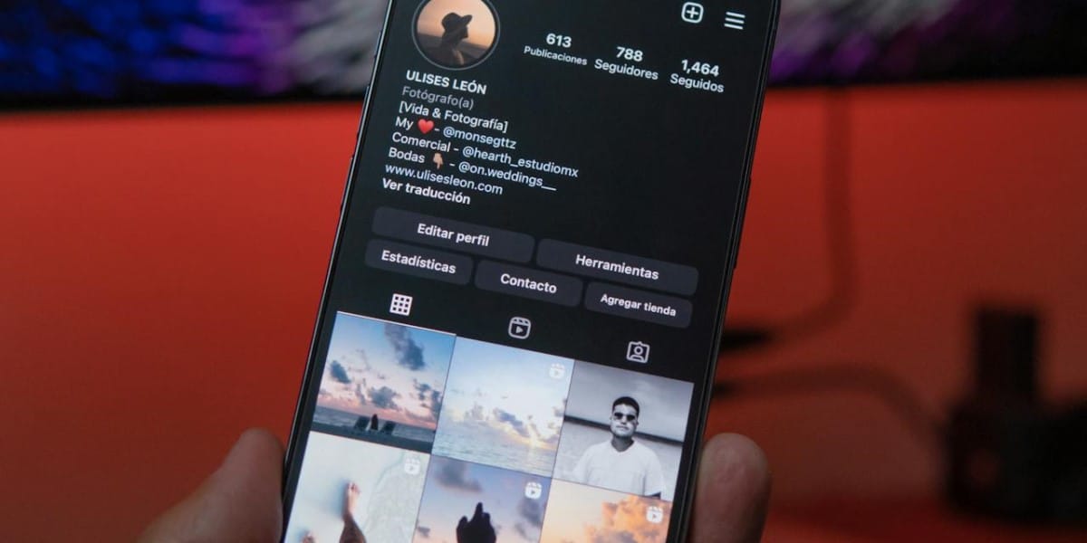 Usuário com celular na mão, a tela está ligada e mostra um perfil no Instagram. O fundo é um local pouco iluminado, com o que parece ser uma parede laranja. Fontes do Instagram.
