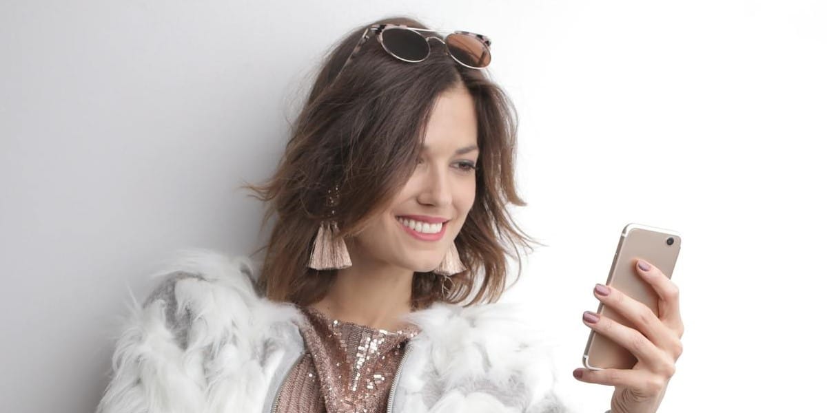 Jovem mulher bem arrumada, segurando seu telefone, sorrindo enquanto faz downloads do Instagram, com um dos aplicativos para baixar Status do Instagram.