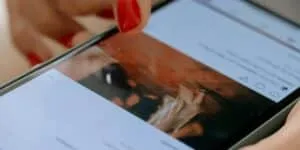 Detalhe mostrando mãos femininas segurando um celular, prestes a tocar com o dedo sobre a tela de um post com foto e comentários. Como apagar comentário no Instagram