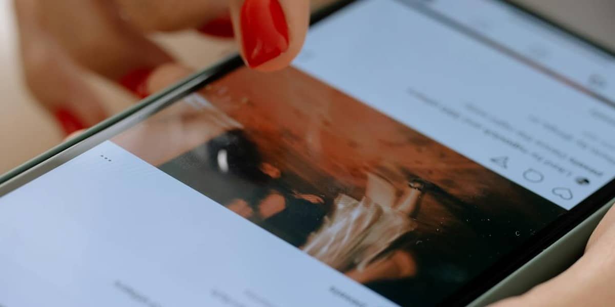 Detalhe mostrando mãos femininas segurando um celular, prestes a tocar com o dedo sobre a tela de um post com foto e comentários. Como apagar comentário no Instagram
