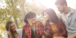 Grupo de 4 amigos, dois homens e duas mulheres, com roupas casuais, ao ar livre, sorrindo e conversando. Uma das jovens segura um celular na mão. Como criar um grupo no Instagram.