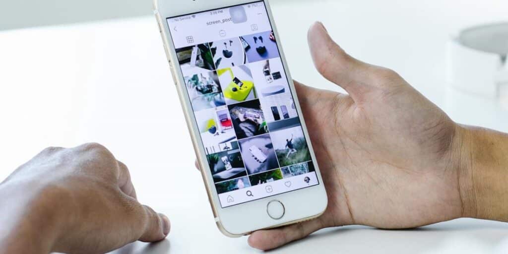 Detalhe mostrando mãos de uma pessoa segurando um iPhone, com tela ligada na página do perfil do Instagram. Como programar stories Instagram.