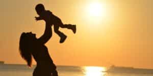 Mãe erguendo seu filho pequeno na praia ao por do sol, foto contra luz. Declaração de amor infantil.