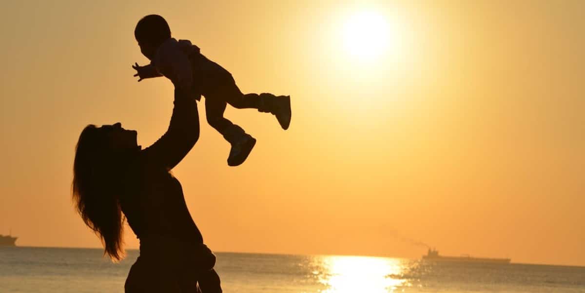 Mãe erguendo seu filho pequeno na praia ao por do sol, foto contra luz. Declaração de amor infantil.