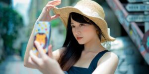 Jovem de pele clara e cabelos escuros, usando chapéu de palha, tira selfie em ambiente urbano ensolarado. Como trocar a foto do perfil do Instagram.