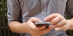Detalhe mostrando jovem com camisa xadrez segurando o celular, enquanto pesquisa se é possível descobrir Instagram pelo número.