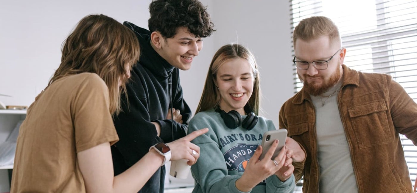 4 jovens em pé no quarto, dois rapazes e duas moças, uma delas segura um celular e sorri. Todos olham para a tela empolgados, comprando seguidores TikTok
