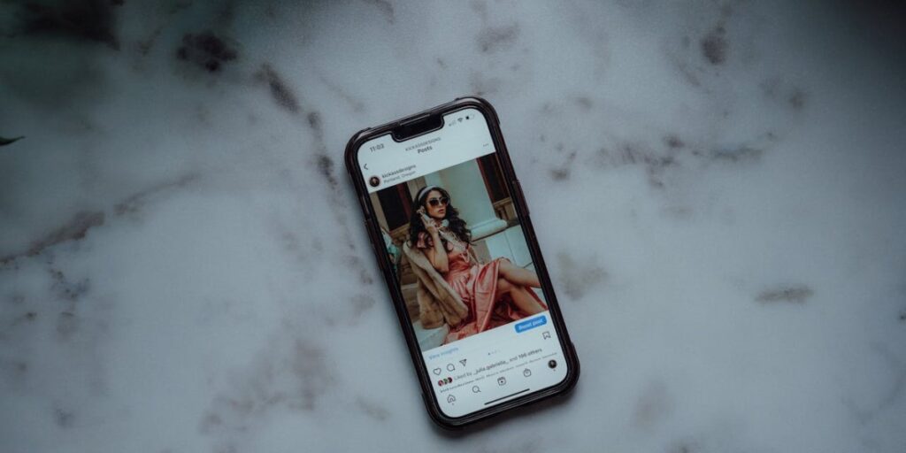 Celular sobre bancada de mármore claro, com tela ligada exibindo post do Instagram de influenciadora bem-vestida, com botão turbinar post logo abaixo da publicação. Como turbinar publicação no Instagram.