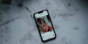 Celular sobre bancada de mármore claro, com tela ligada exibindo post do Instagram de influenciadora bem-vestida, com botão turbinar post logo abaixo da publicação. Como turbinar publicação no Instagram.
