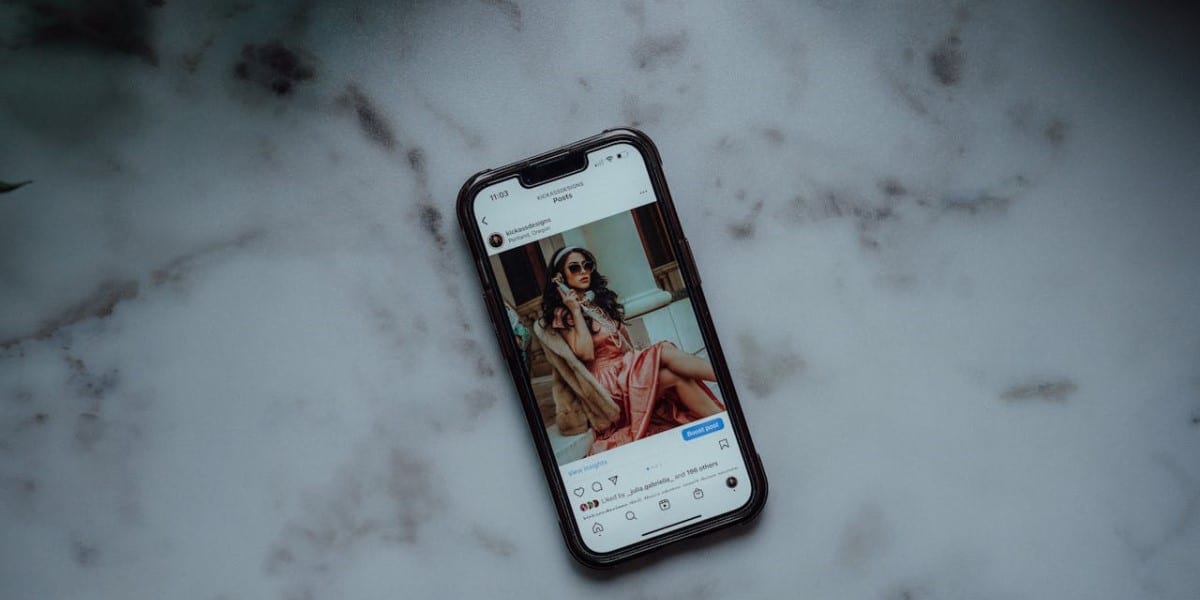 Celular sobre bancada de mármore claro, com tela ligada exibindo post do Instagram de influenciadora bem-vestida, com botão turbinar post logo abaixo da publicação. Como turbinar publicação no Instagram.