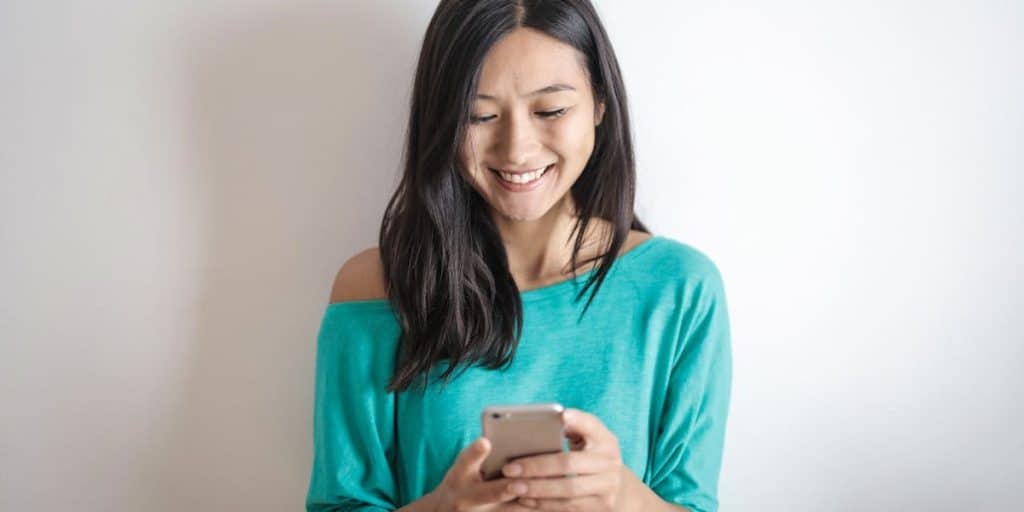 Jovem sorrindo com celular na mão enquanto aprende acompanha os seguidores Instagram sendo repostos