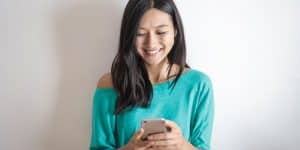 Jovem sorrindo com celular na mão enquanto aprende acompanha os seguidores Instagram sendo repostos