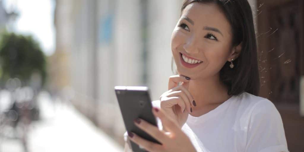 Jovem sorrindo com celular na rua, olhando para cima pensando em algo bom sobre prazos e garantias para reposição de seguidores