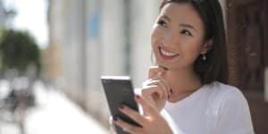 Jovem sorrindo com celular na rua, olhando para cima pensando em algo bom sobre prazos e garantias para reposição de seguidores